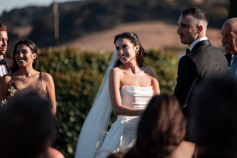 Couple sharing an intimate moment during outdoor wedding ceremony with guests in background.