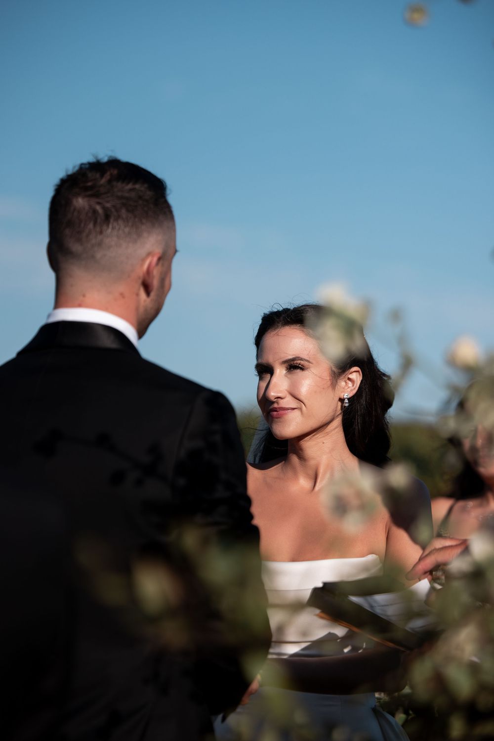 Close-up profile shots of bride and groom during sunset wedding ceremony against blue sky.