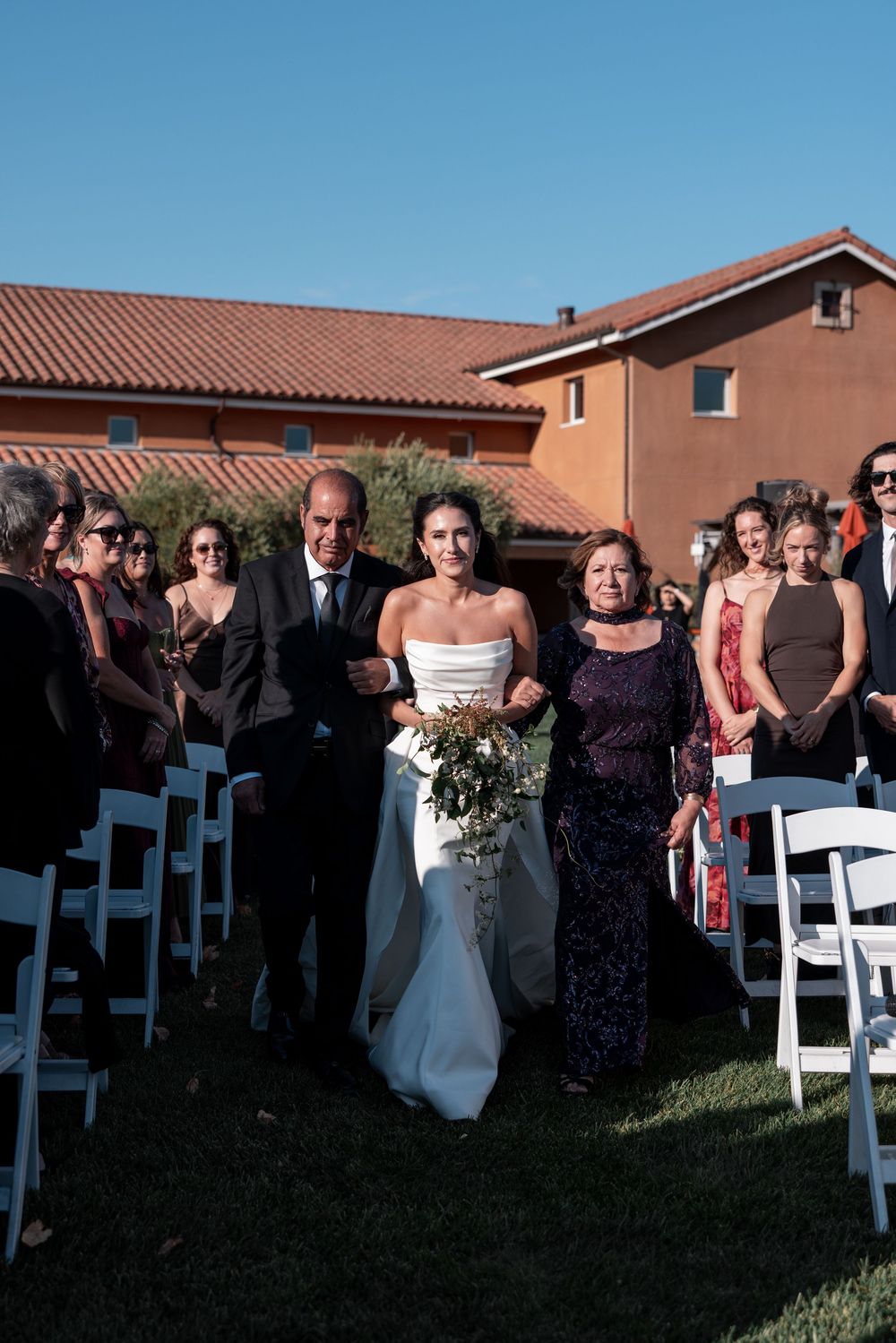 A wedding ceremony setup outdoors with white chairs and buildings in the background during sunset.