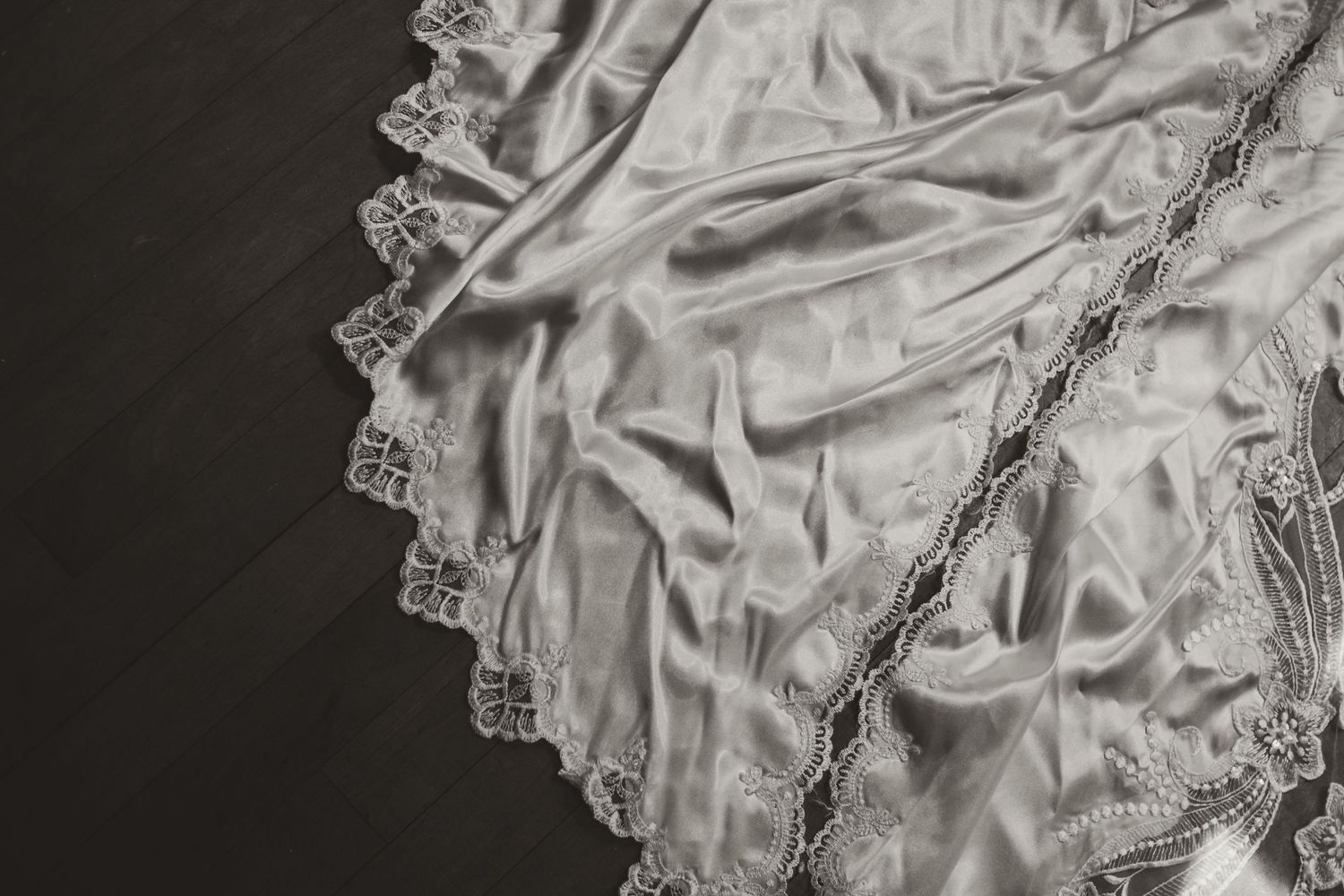 Elegant white satin fabric with delicate lace trim draped on dark wood surface.