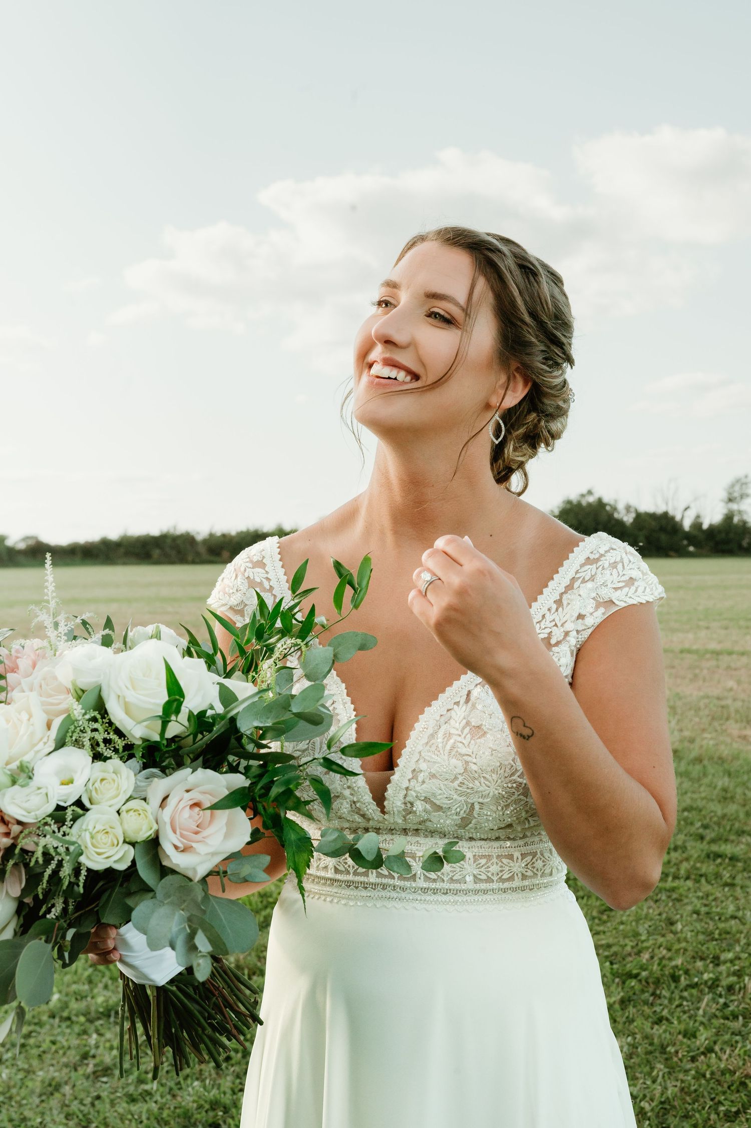 Smiling bride in lace wedding dress holding white and green bouquet outdoors on a sunny day in Slinger, Wisconsin.
