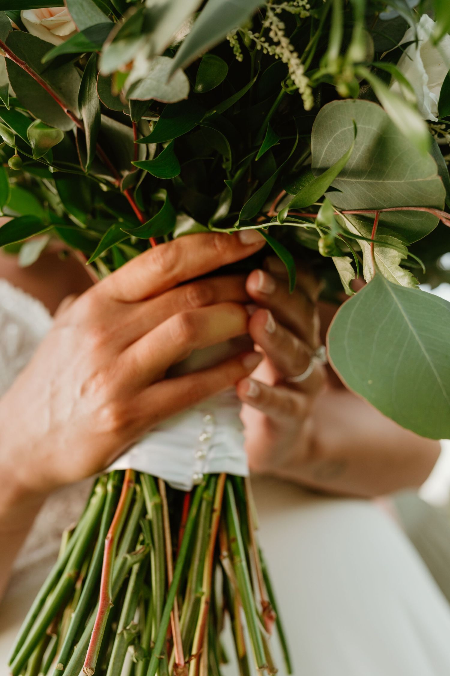 Bride holding a lush green eucalyptus wedding bouquet with stems wrapped in white ribbon.