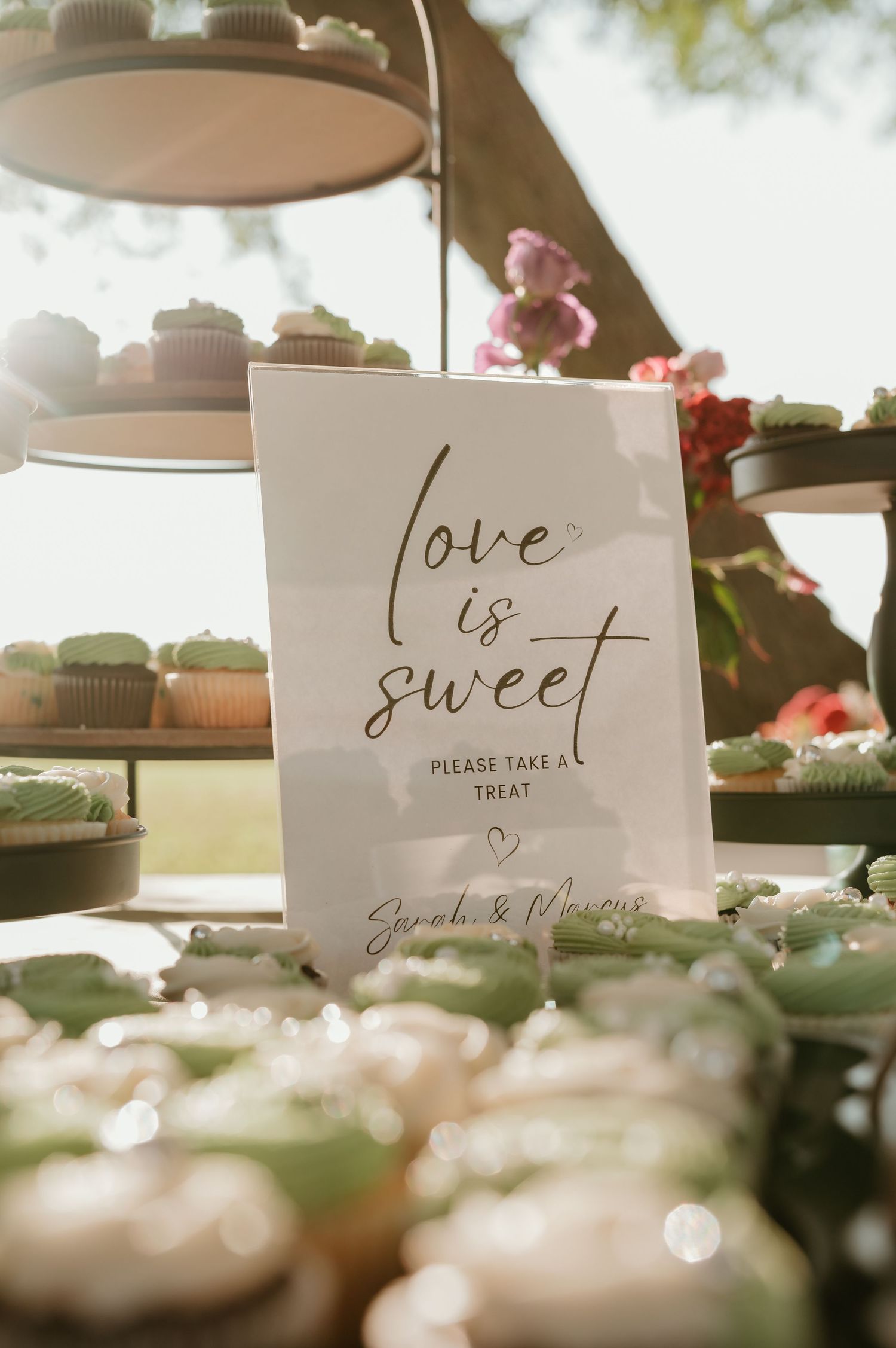 Wedding dessert table with a sign reading love is sweet please take a treat, surrounded by cupcakes and macarons.