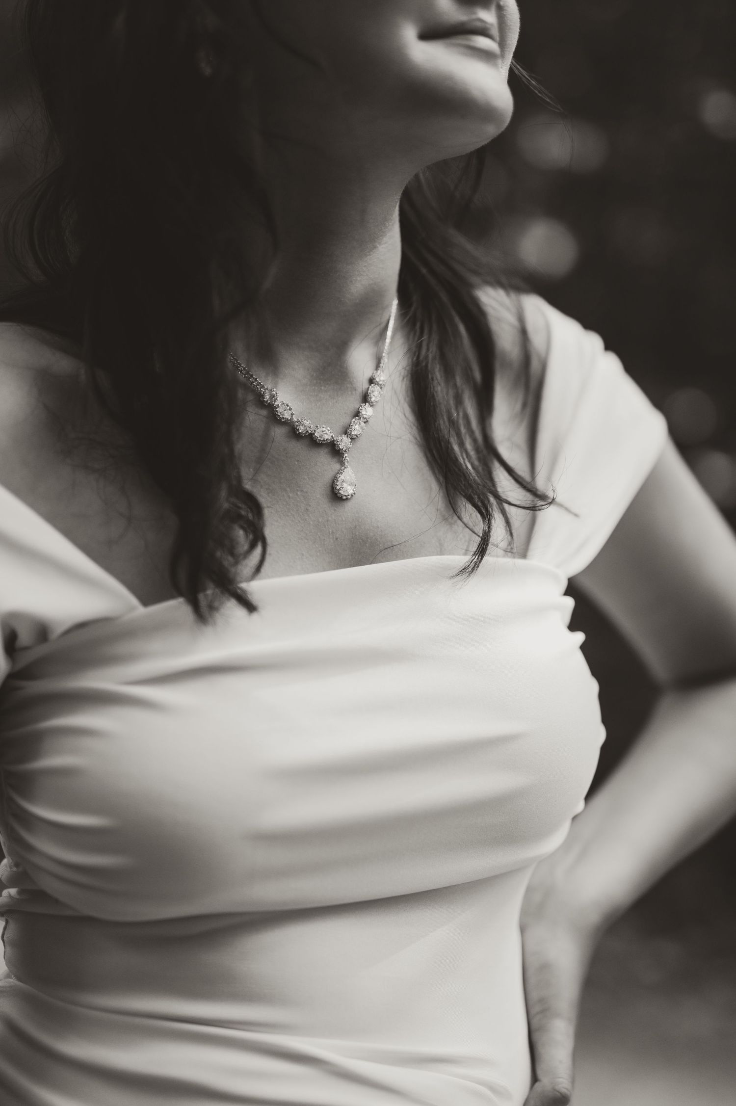 Black and white photo of a bride in a strapless white gown wearing a delicate pearl necklace, smiling softly.