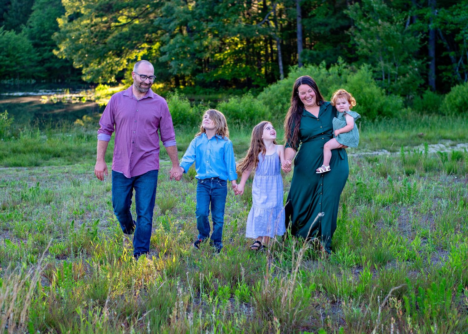 A group walks together through a wildflower meadow at sunset with green forest in the background.