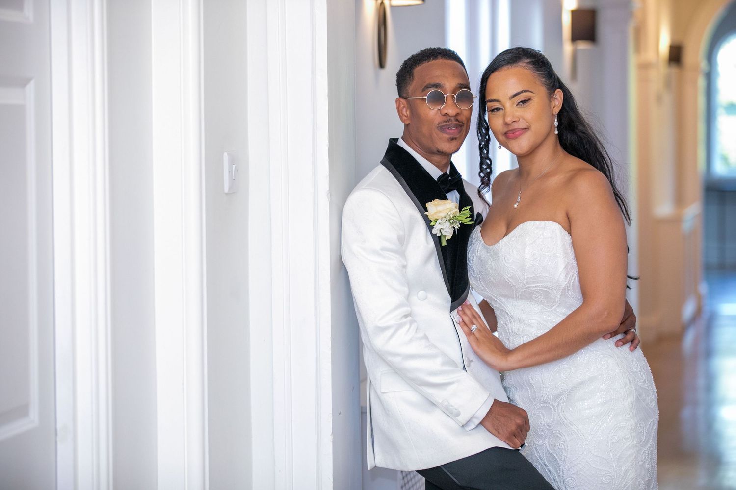 A couple poses in a bright hallway, exuding joy and elegance.