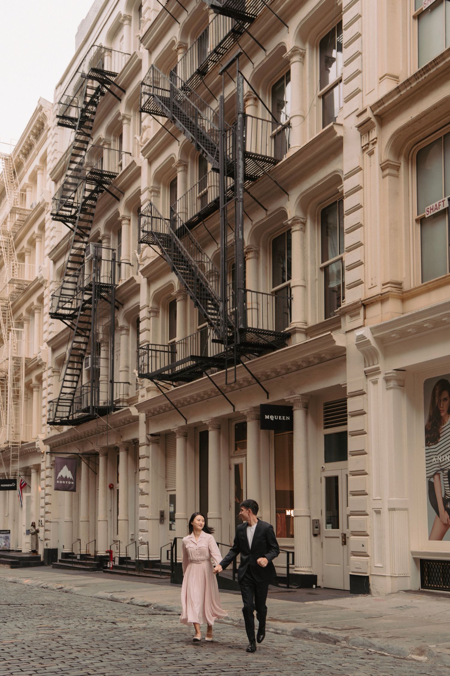 Romantic couple walking through historic SoHo architecture with fire escapes and columns.