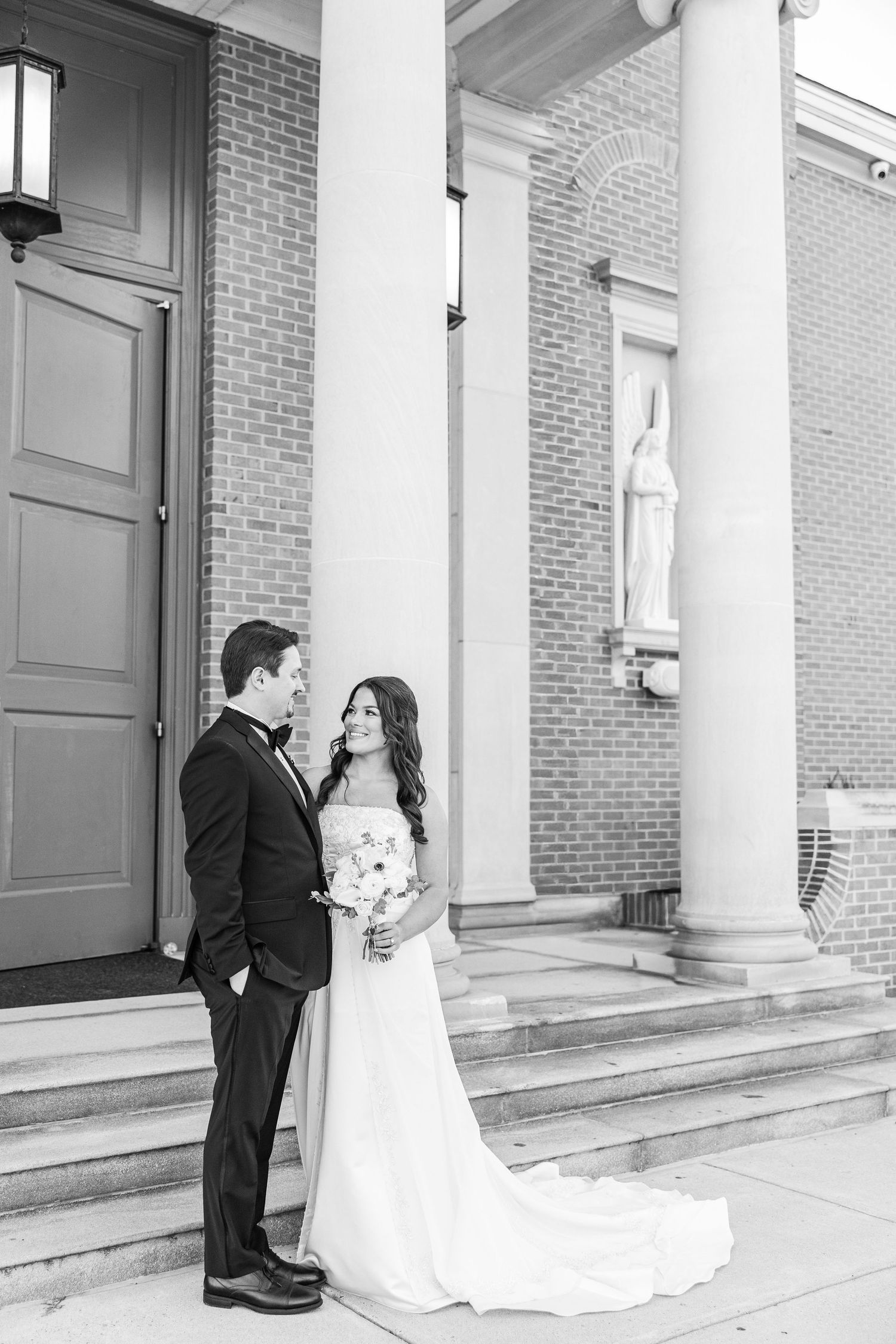 A black and white wedding photo sequence showing a couple sharing romantic moments on a columned brick building porch.