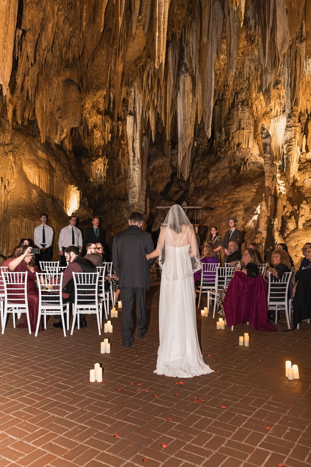 Wedding ceremony setup inside a dramatic limestone cave with white chairs and glowing candle lanterns lining the aisle.