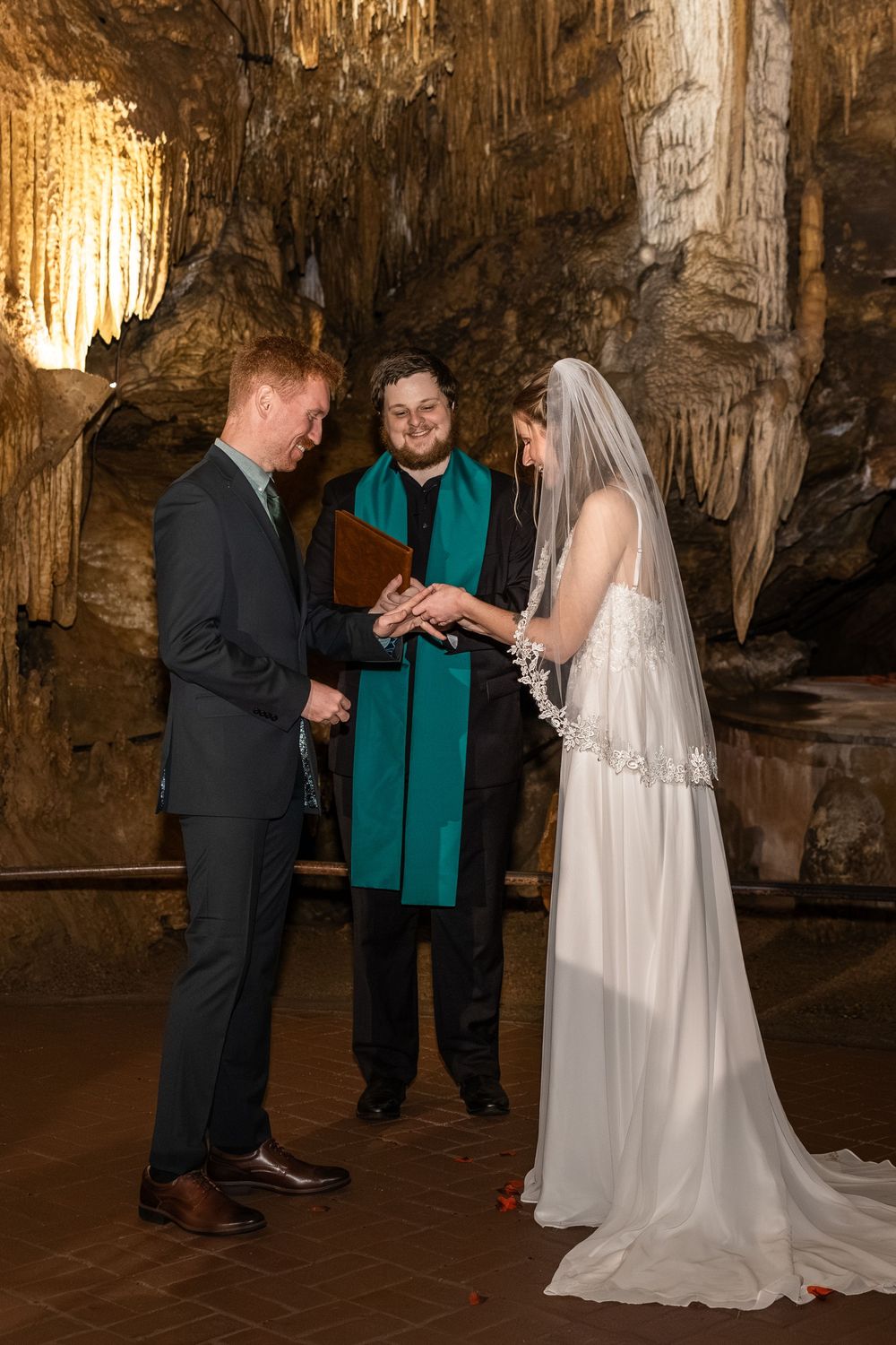 A wedding ceremony taking place inside a dramatic natural cave with illuminated stalactites and limestone formations.