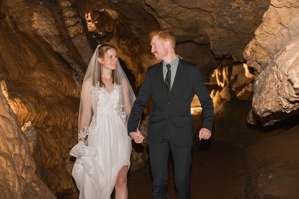 Wedding ceremony taking place in a stunning cave setting with dramatic stalactites and warm lighting.