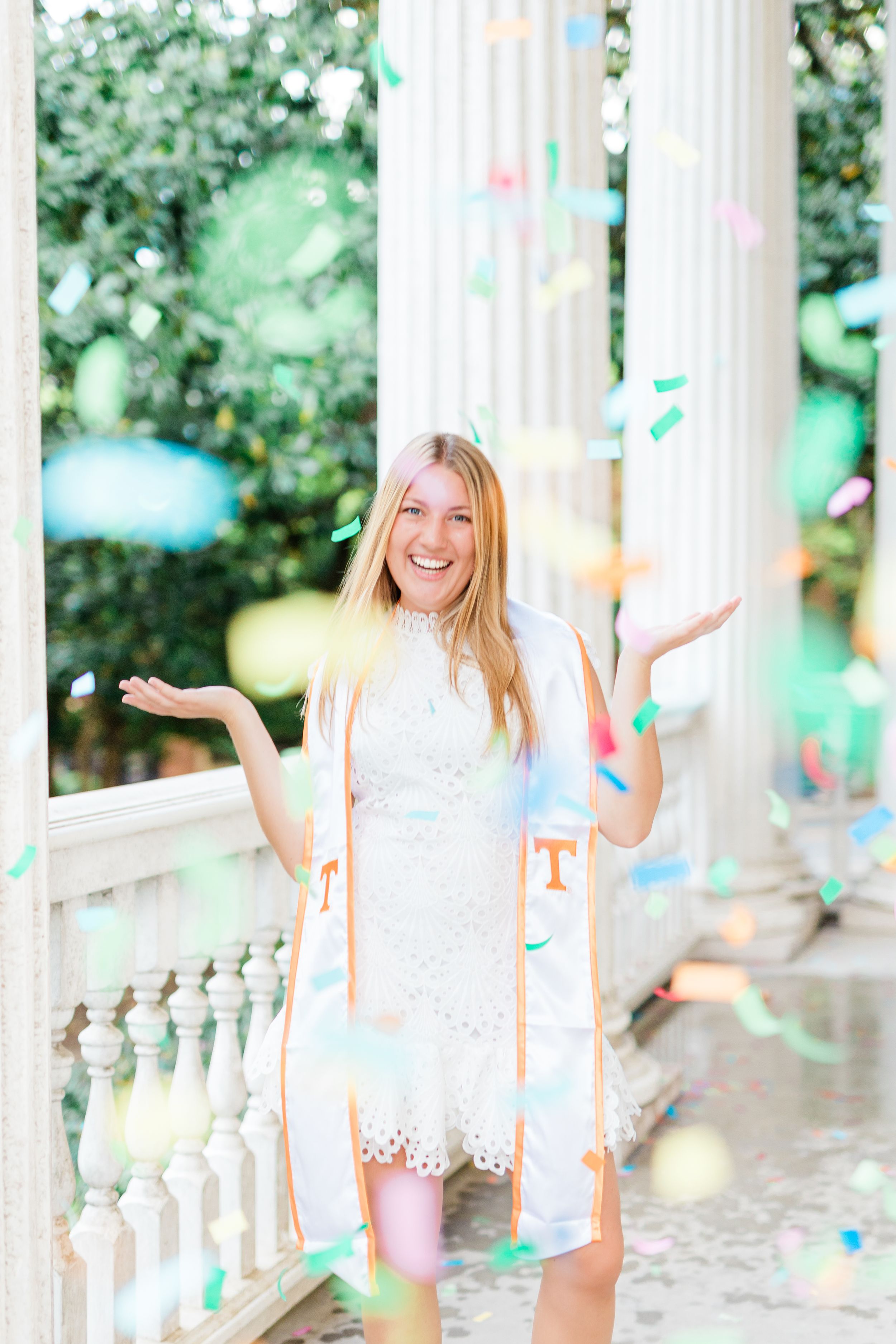 White lace dress and confetti create a joyful celebration scene on an elegant porch with classical columns.