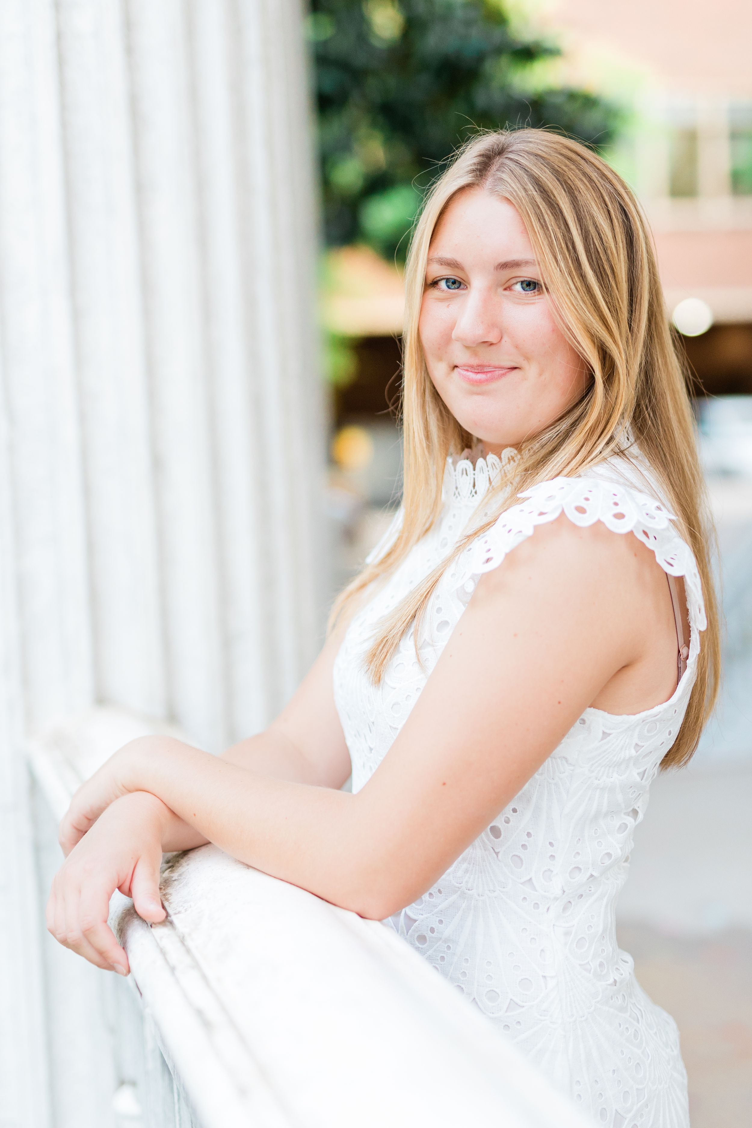 A person in a white lace dress poses outdoors against white columns for a portrait session.