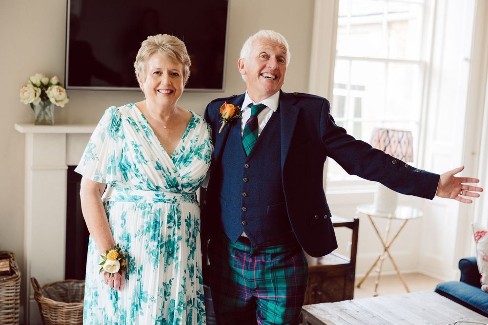 A couple in formal attire, with a turquoise dress and dark suit, share a joyful moment in a bright indoor setting.