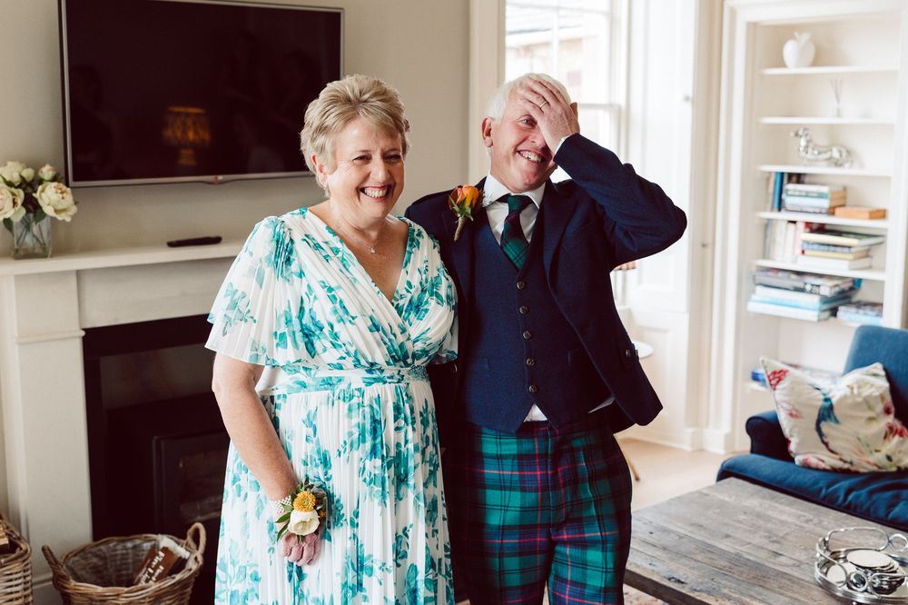 A couple in formal attire, with a turquoise dress and plaid suit, share joyful moments together in a bright indoor setting.