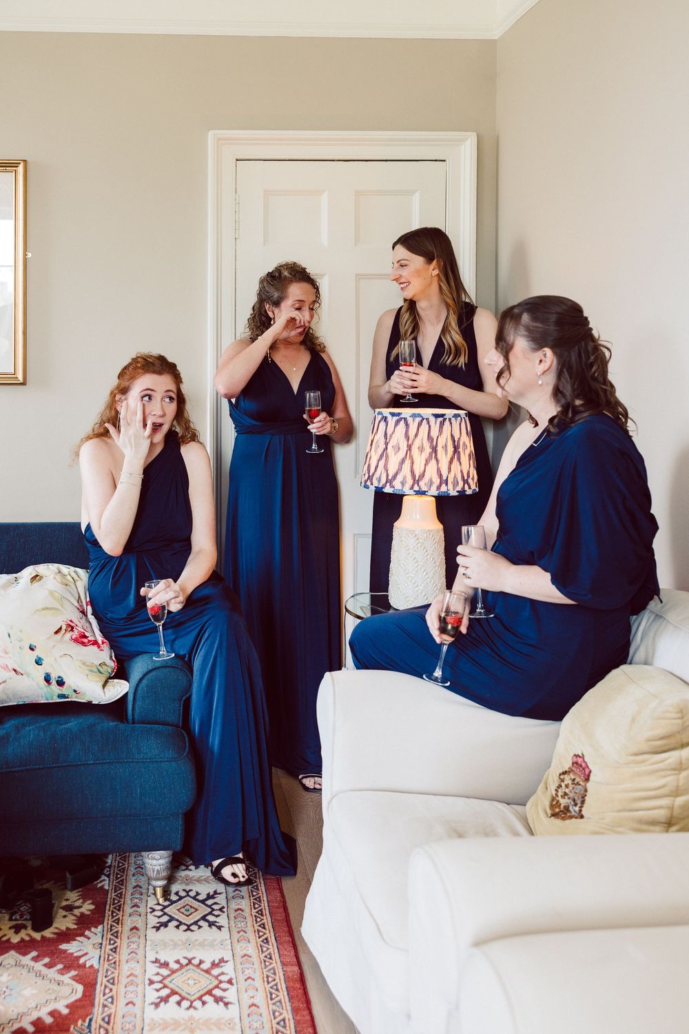 Friends laughing together on a white sofa with a patterned rug in a bright interior setting.