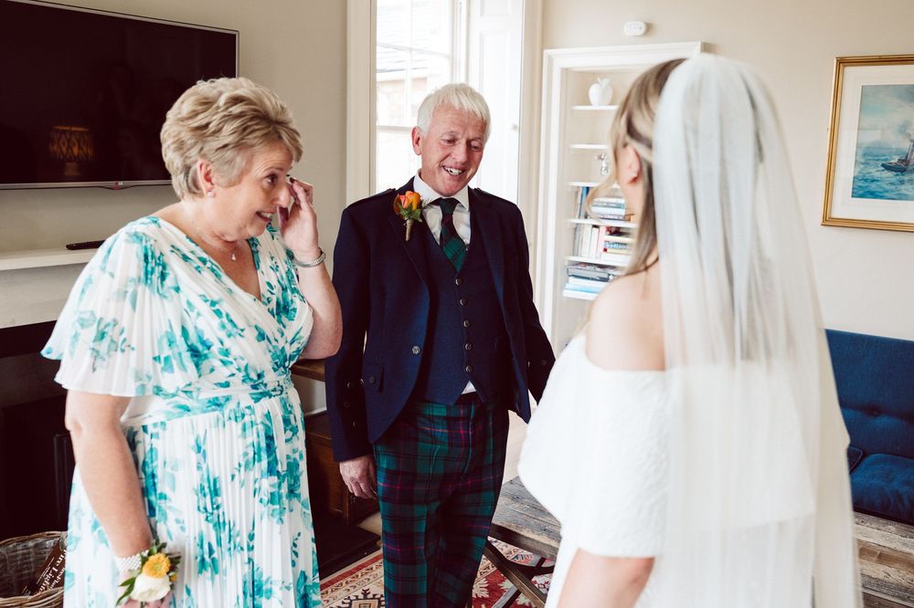 A bride in a white wedding dress and veil shares a joyful moment with guests in formal attire at a wedding.