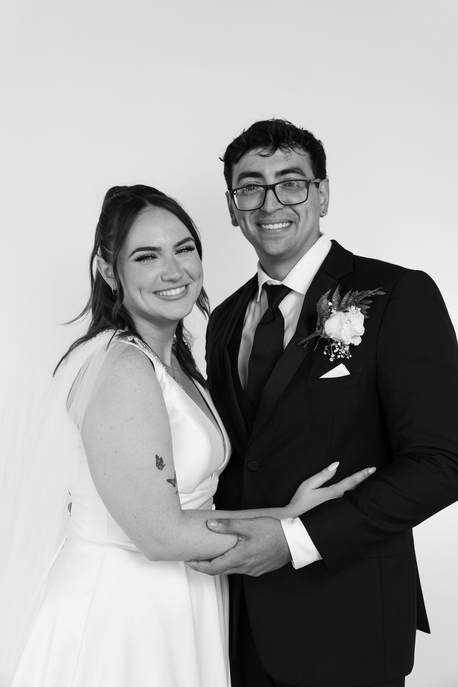 A black and white wedding portrait of a couple in formal attire smiling at the camera.