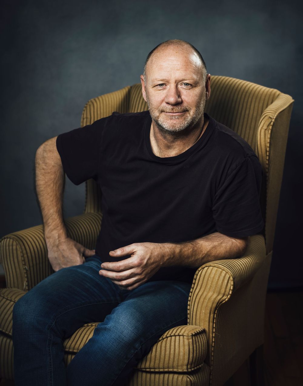 A studio portrait of a man sitting on an arm chair. Fine art portrait photography.