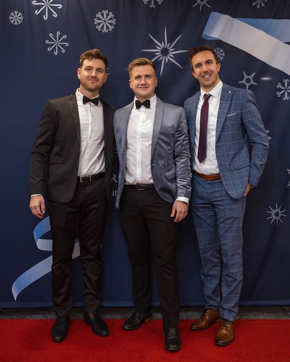 Formal group photo of attendees in suits against decorative winter backdrop with snowflake designs.