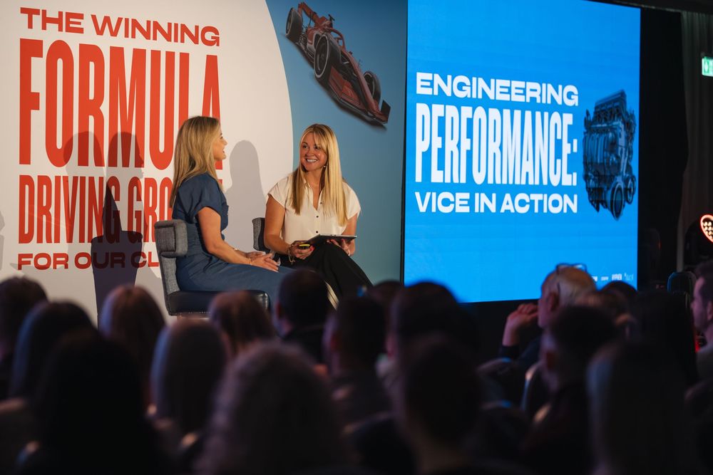 Two women on stage at a conference with screens displaying Engineering Performance and The Winning Formula presentations.