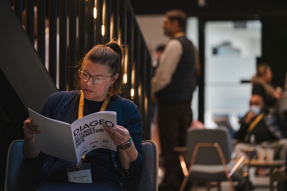 Conference attendees reading materials in a darkened auditorium with warm lighting.