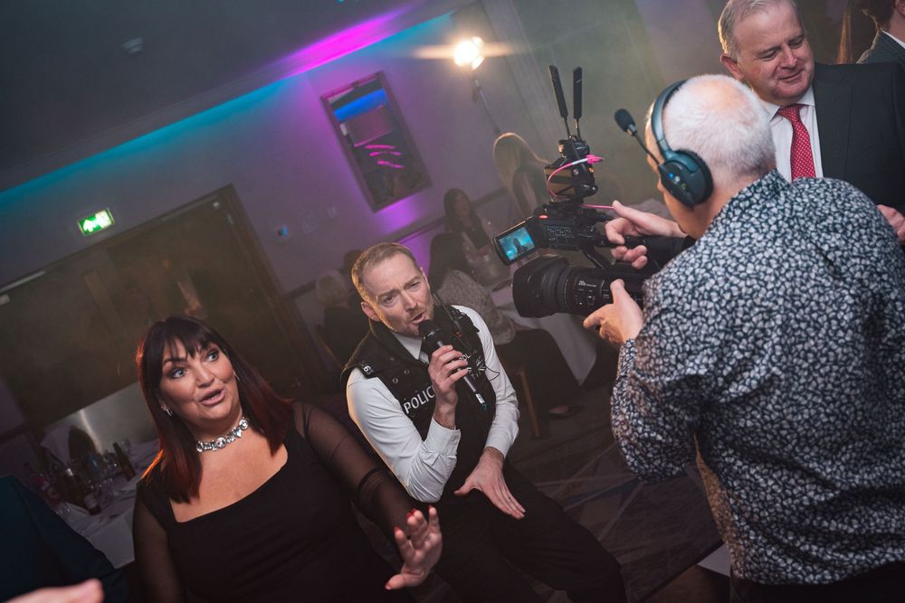 Party guests dancing and celebrating under colorful nightclub lights with drinks in hand.