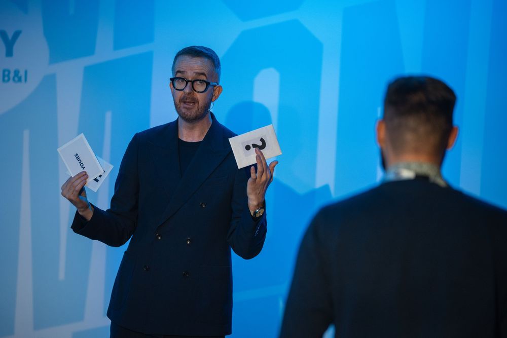 Presenter speaking on stage at a corporate event with blue lighting and Suntory branding in the background.