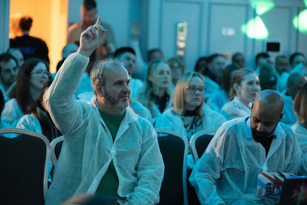 Large crowd of spectators seated in rows under cyan-tinted lighting during an indoor event.