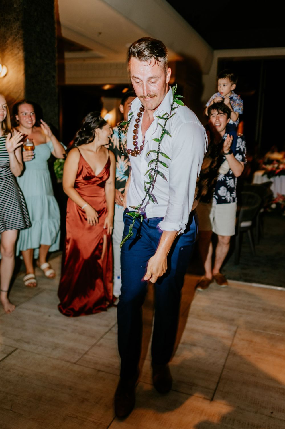 Guests dancing energetically at wedding reception on wooden dance floor.