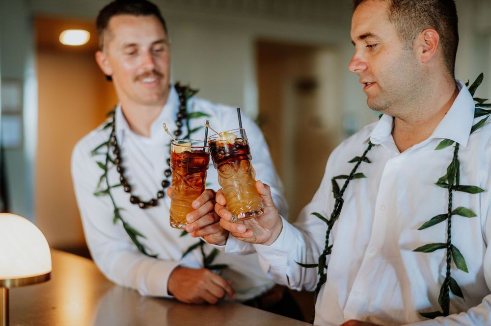 Wedding party members wearing traditional Hawaiian maile leis toast with drinks.