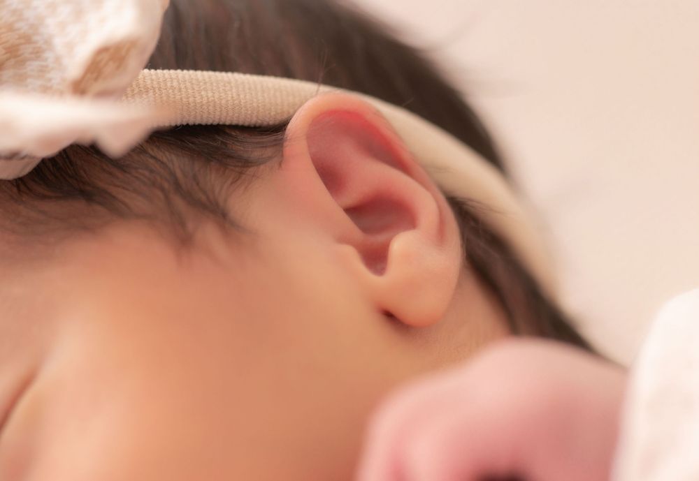 Close-up of a sleeping baby's ear with a soft headband, showcasing delicate infant features.