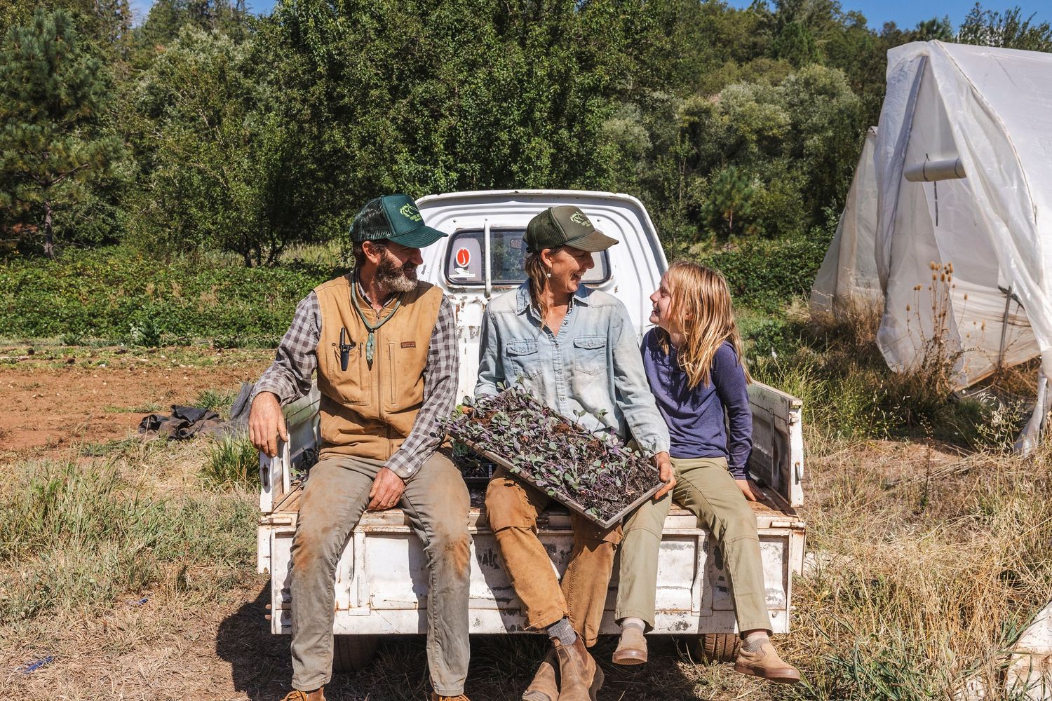 A group of people sit in the back of a pickup truck while traveling through a rural countryside setting.
