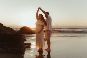 A romantic couple shares a tender moment on the beach at sunset with the ocean waves rolling in the background.
