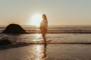 A silhouetted figure walks along a misty beach at sunset with waves crashing against the shore.