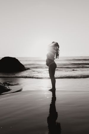 A silhouetted figure bends down on a misty beach at sunset creating a dramatic reflection on the wet sand.