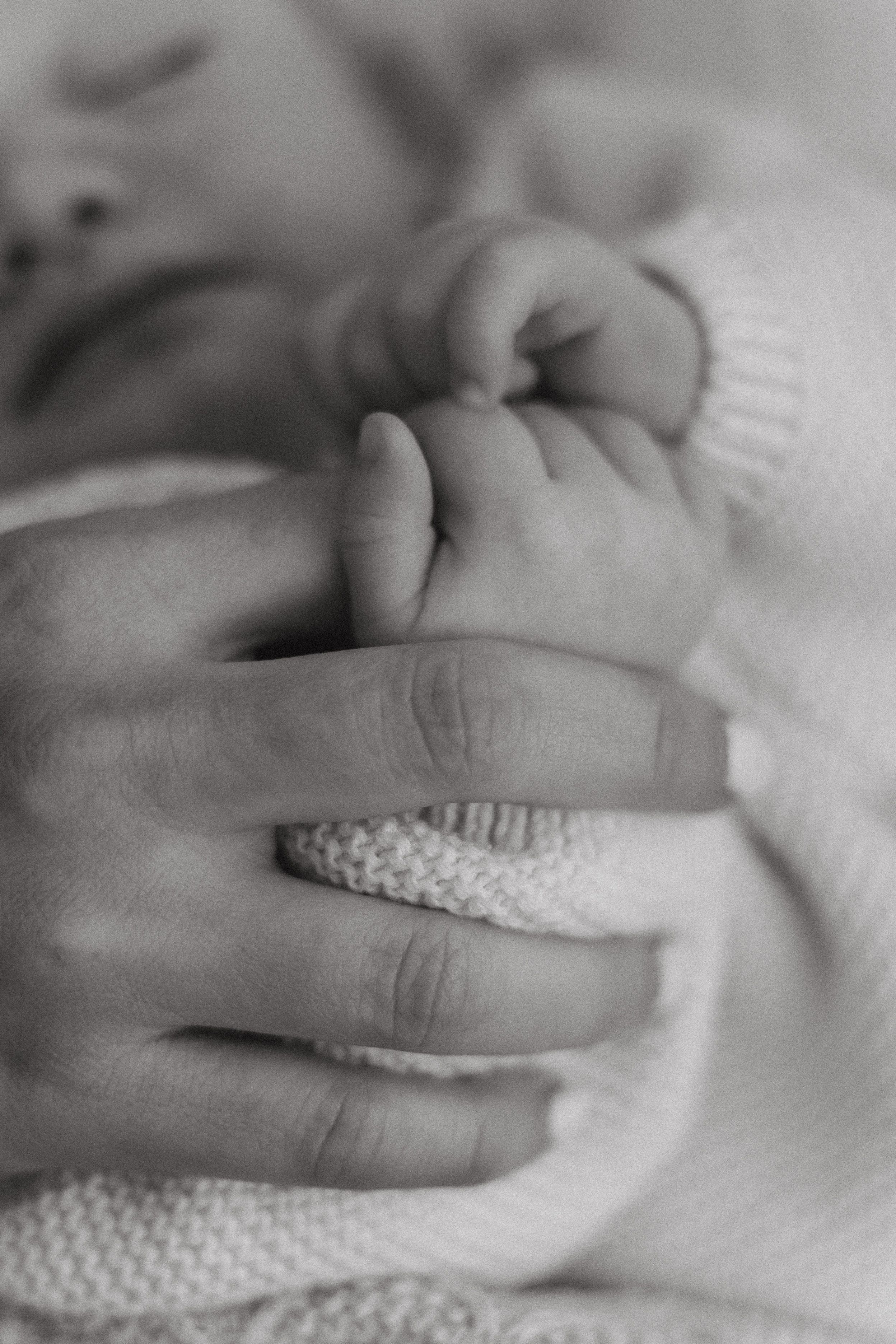 A series of black and white close-up photographs showing gentle baby hands touching soft knitted fabric.