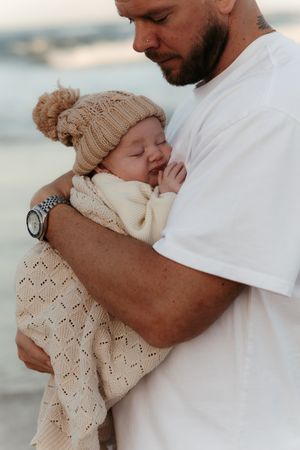 A tender moment at the beach shows a baby in a knit hat being cradled in protective arms.