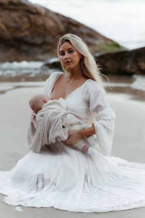 A dreamy beach photoshoot featuring flowing white lace dresses against rocky coastal backdrop at sunset.