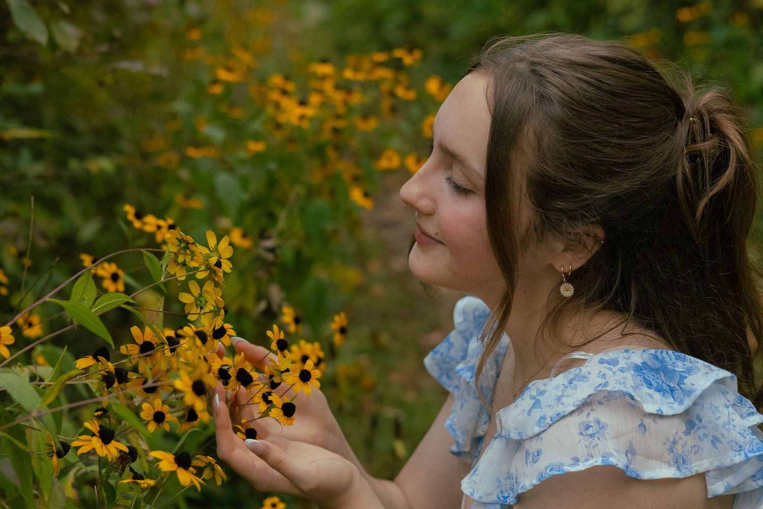 A person in a blue ruffled dress stands in a garden filled with vibrant yellow and orange wildflowers during her senior photos in Michigan.