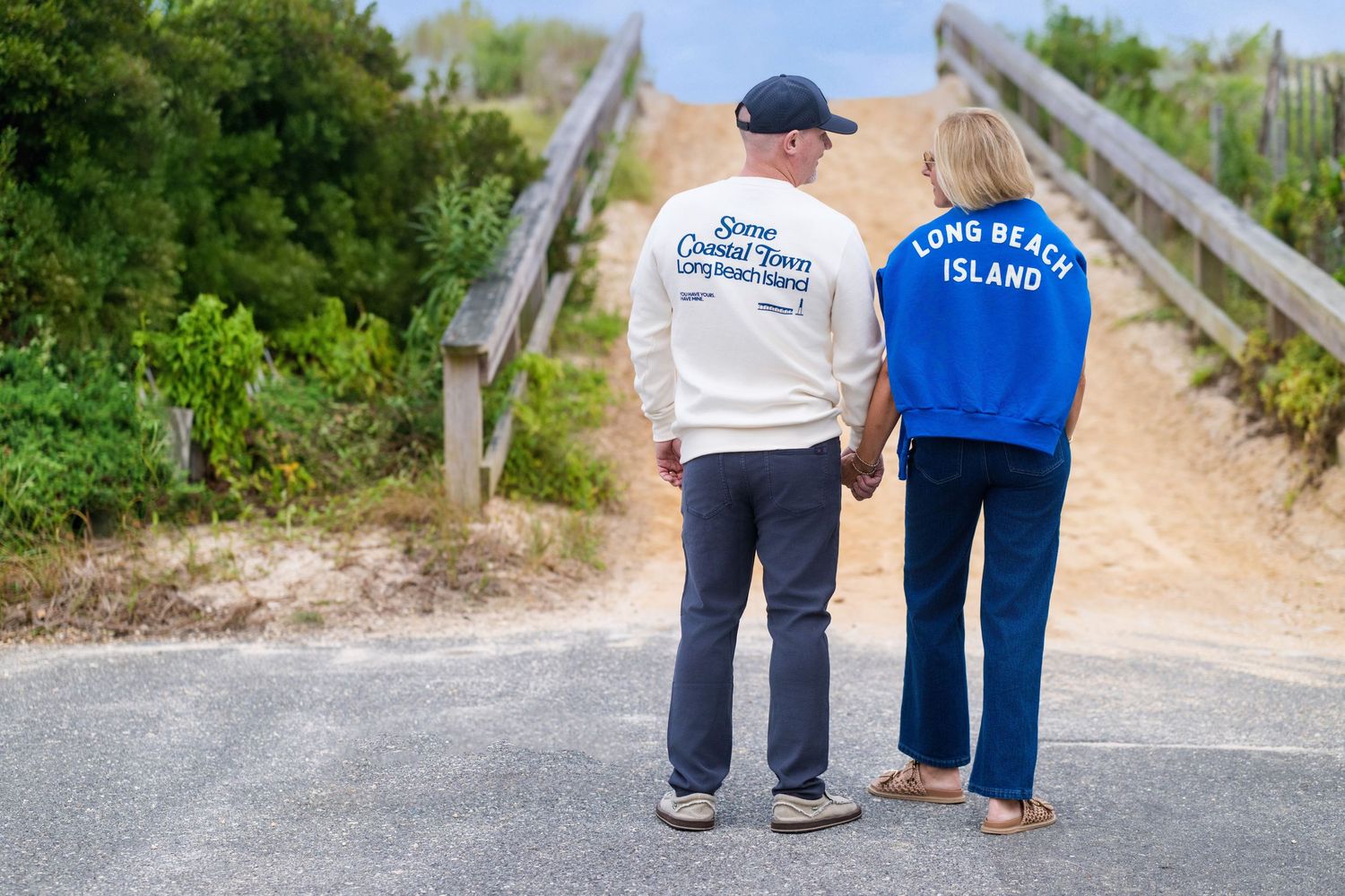 Two people wearing sweatshirts walking together on a beach boardwalk path.