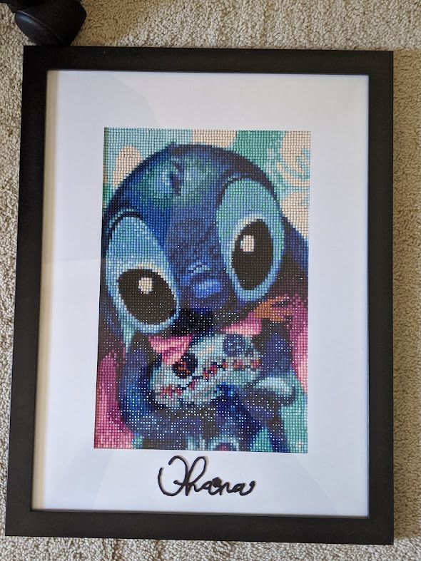 Cross-stitch artwork of Stitch character from Lilo & Stitch in blue watercolor style with frame.