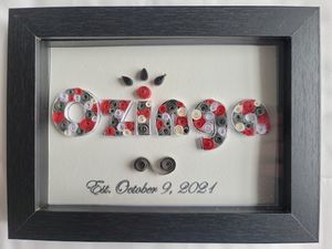 Framed paper quilling artwork spelling 'Ozinga' with decorative floral patterns dated October 9, 2021.