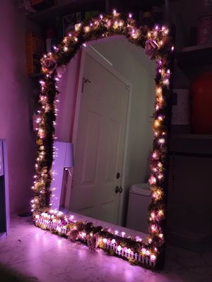 Large mirror with twinkling fairy lights and floral decorations wrapped around its frame creating a magical glow.