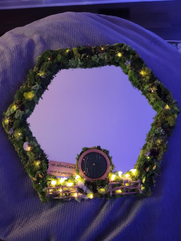 Hexagonal mirror with green moss and LED lights creating an enchanted forest frame effect.