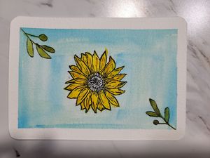 Cheerful watercolor painting of a yellow sunflower with green leaves against a light blue background.
