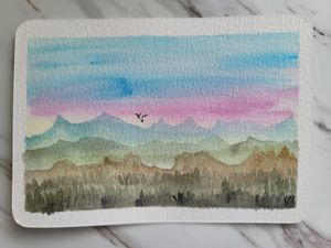 Landscape watercolor with pink and blue sky over rolling mountains and forest silhouettes.
