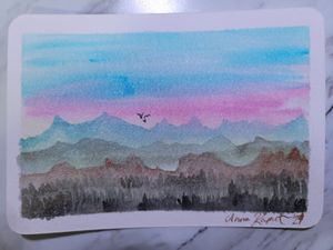 Watercolor painting of purple and blue mountains at sunset with birds flying in the distance.
