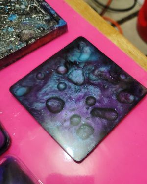 Abstract fluid art tile with purple and blue galaxy-like patterns and bubble effects.
