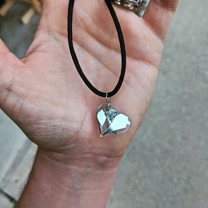 Silver heart pendant on a black cord necklace displayed on palm.